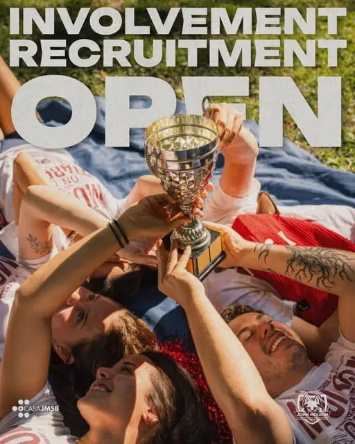 JMCC delegates lying on a blanket on the grass raise a silver trophy together. Involvement Recruitment Open.