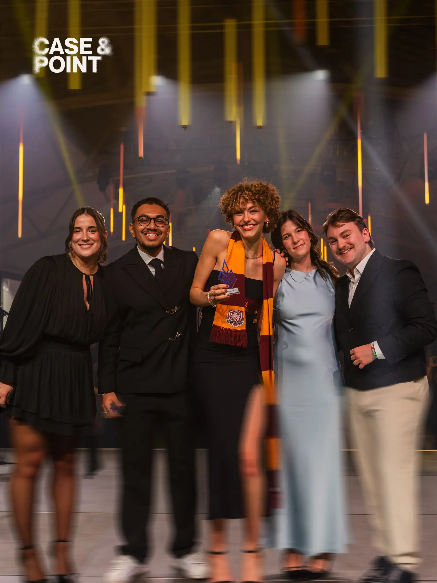 Five JMCC delegates in formal wear posing together on stage under gold lights