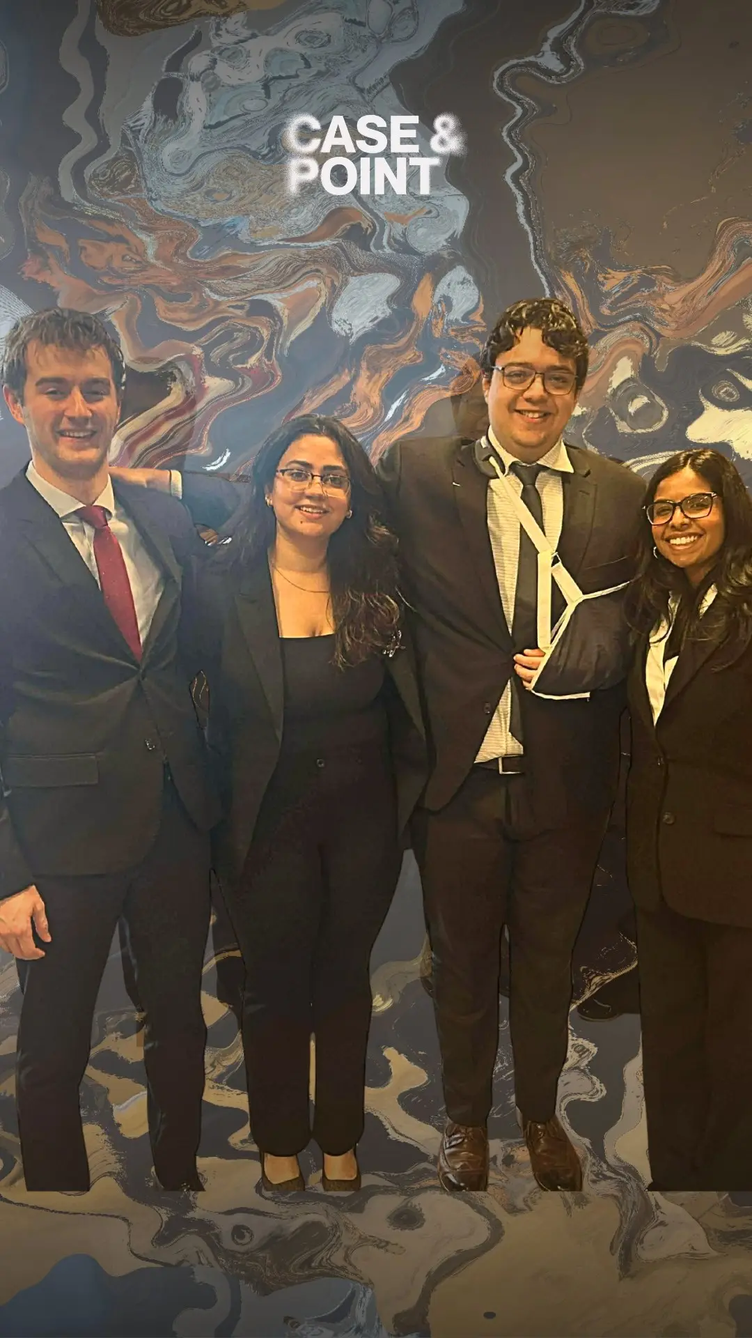 Four JMCC debate delegates in formal wear posing in front of a mural, one holding an award