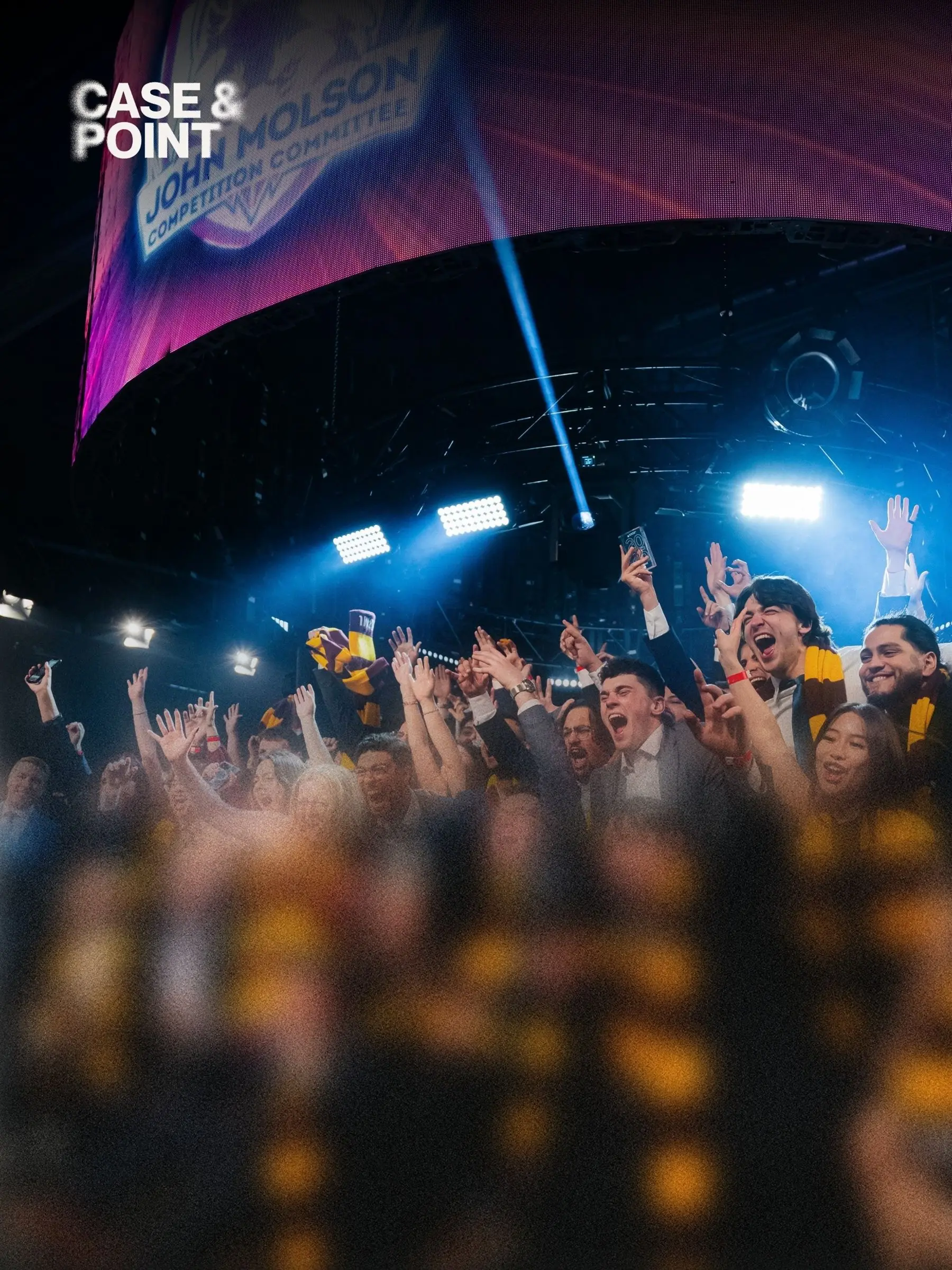 A crowd of JMCC delegates with arms raised in front of a lit arena stage