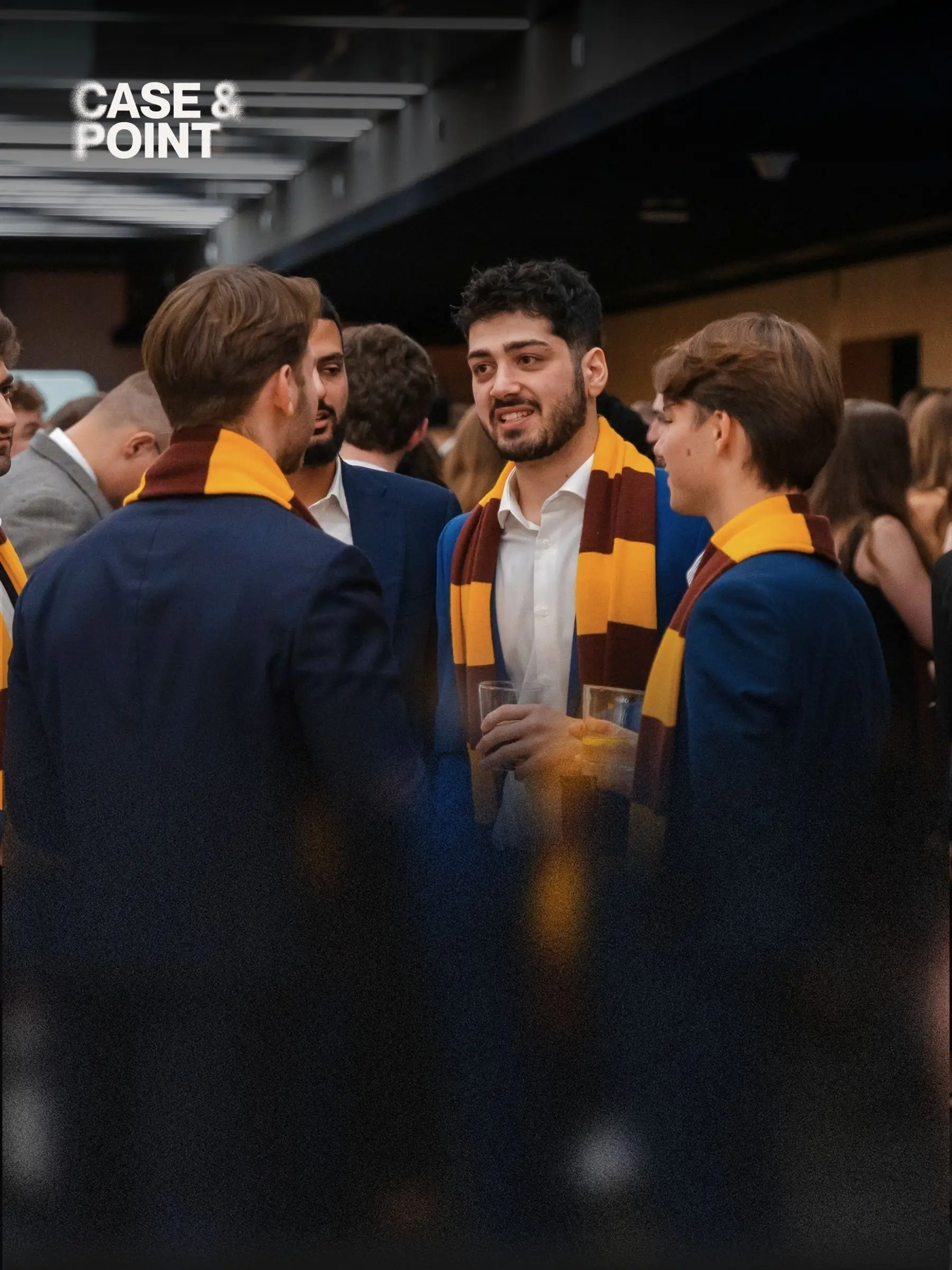 JMCC delegates in blazers and striped JMCC scarves talking together at an indoor reception