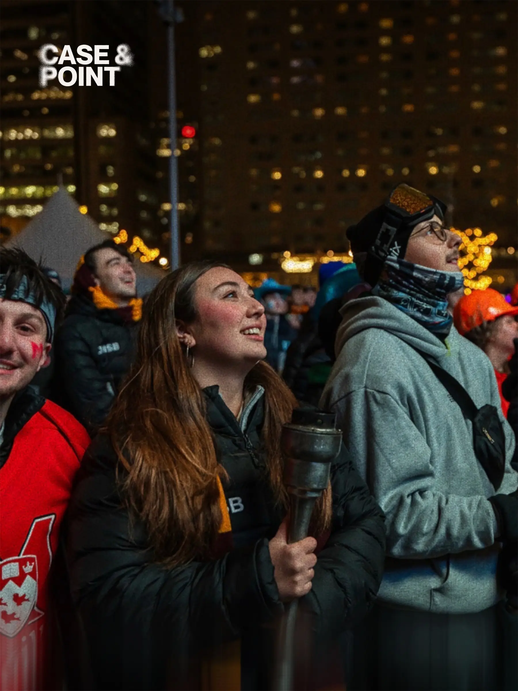 JMCC delegates outdoors at night in winter coats, one carrying a flag, city lights behind them