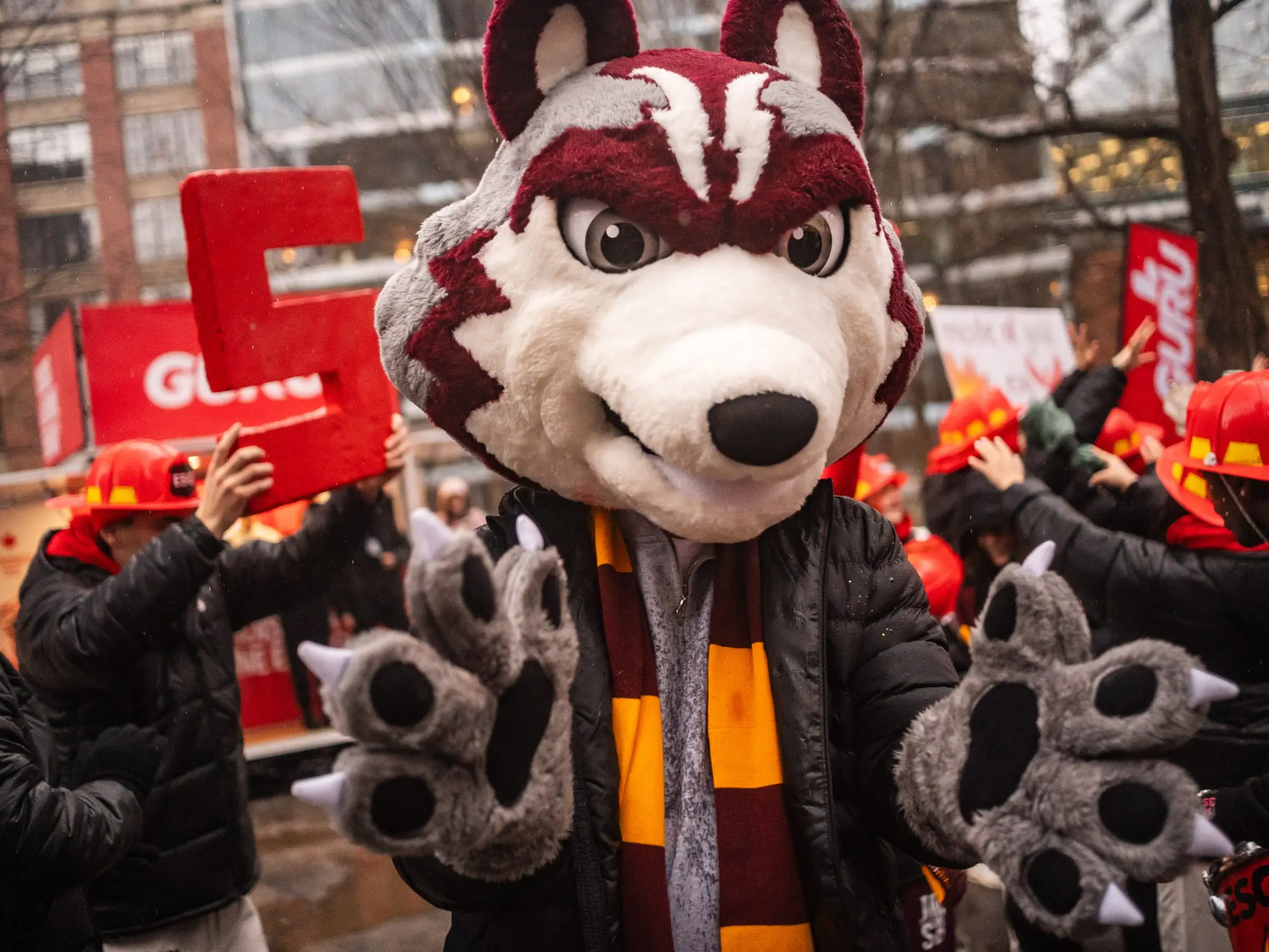 The JMCC wolf mascot reaching both paws toward the camera at the Jeux du Commerce 2026 parade