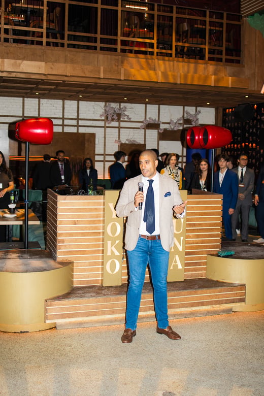 A speaker with a microphone addresses guests at the Golden Hour networking cocktail at Yoko Luna.